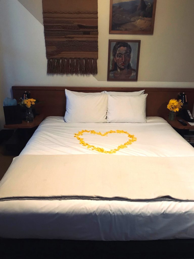 Flowers arrangements on both sides of the bed with a heart made of yellow rose petals in the center at The Freehand Hotel DTLA